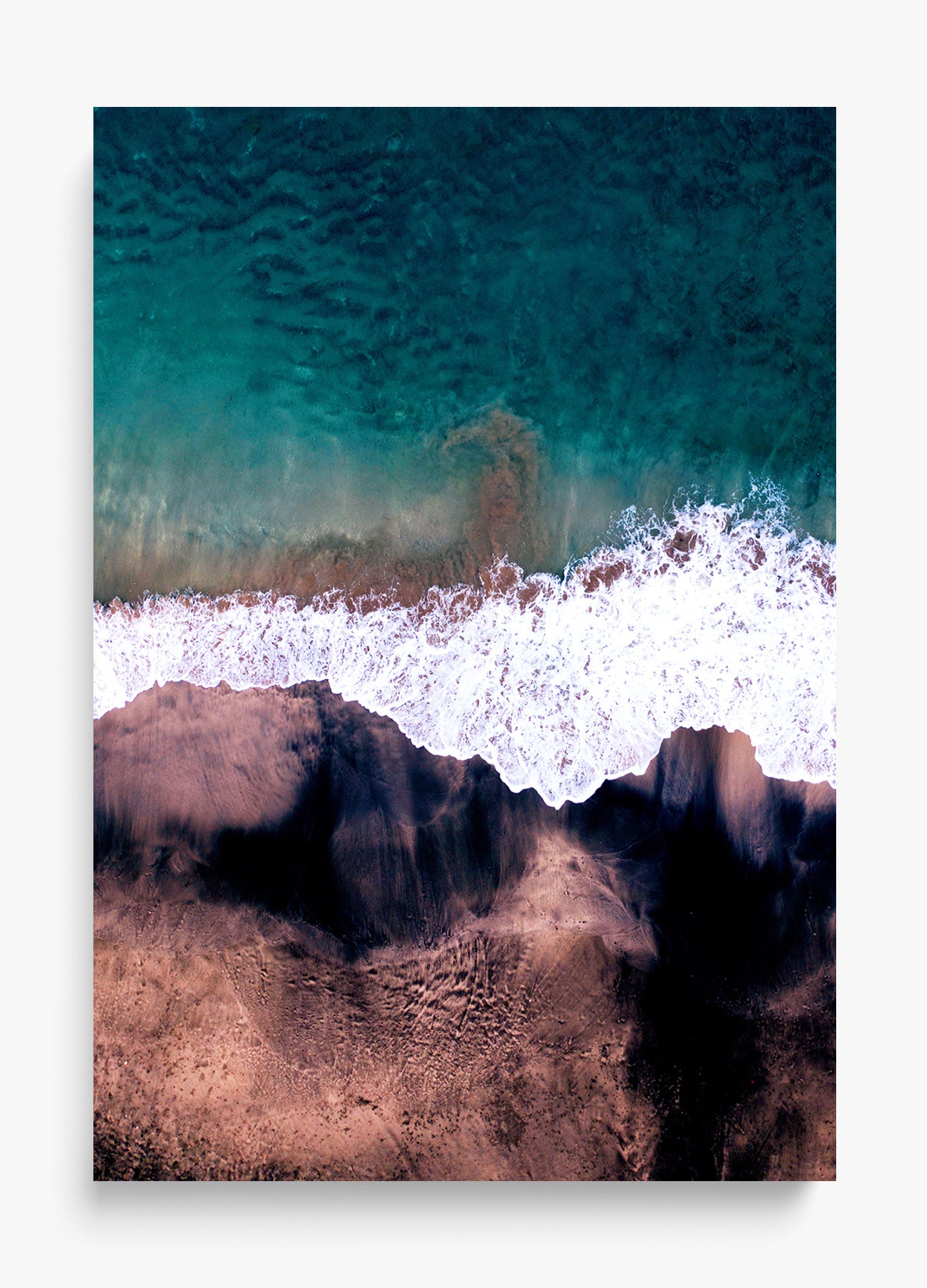 Abstract wall decor featuring a top-down view of a beach with dark sand, turquoise water, and white foamy waves.