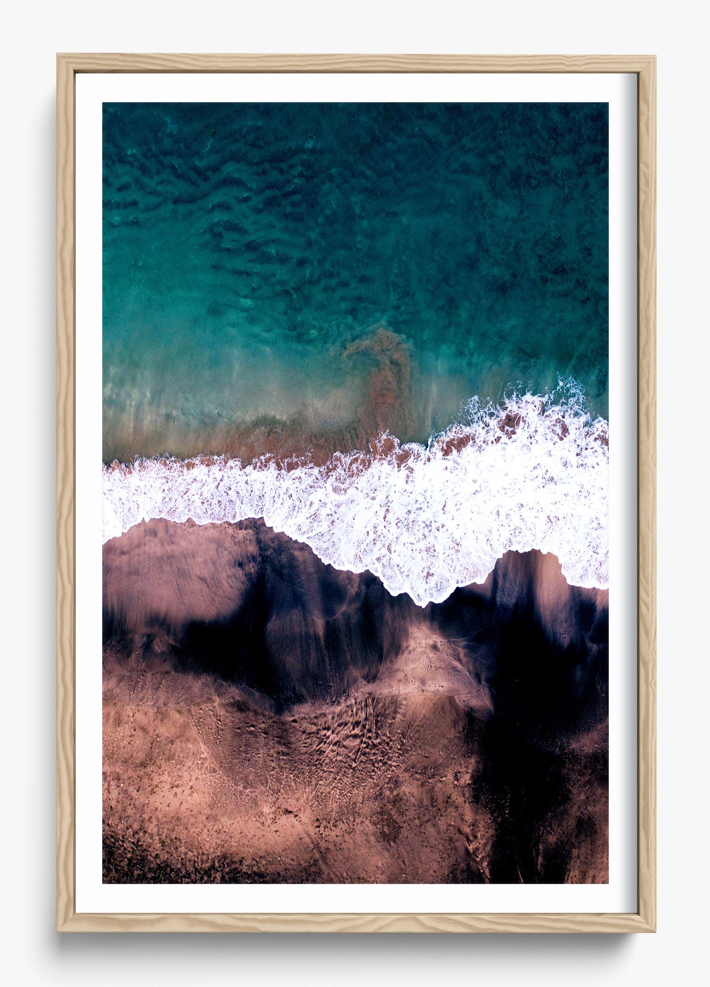 Framed wall decor featuring an aerial view of a beach with blue water and white waves crashing on a sandy shore.